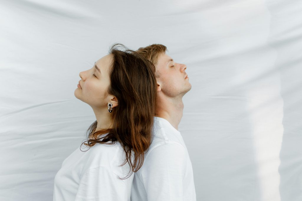 A serene portrait of a man and woman posed back to back on a white background.