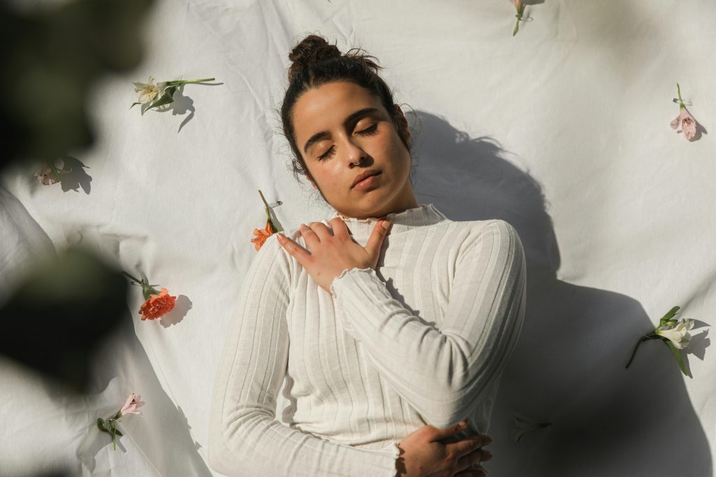 Serene woman with closed eyes in white sweater surrounded by flowers.