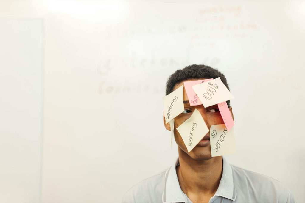 Young man with sticky notes on his face representing creative office thinking and multitasking.